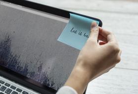 female hand with writing let it be on sheet of paper at laptop