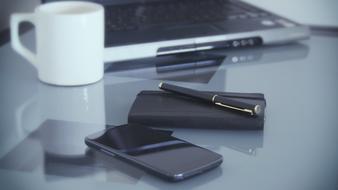 laptop, notebook, pen, smartphone and cup on a glass table