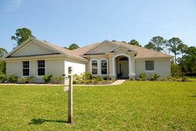 Home in light, with the sign and colorful garden in Florida, under the blue sky, with clouds