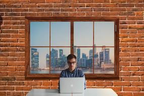 Man with the laptop with brick wall with the window on background