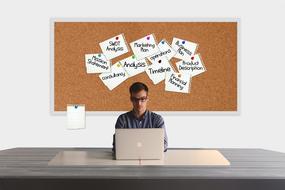 young man works with laptop in front of bulletin board with stickies