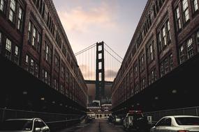 view of suspension Bridge in end of busy street with the cars