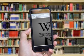 wikipedia symbol on screen of smartphone in front of books on shelves