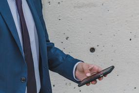 Businessman holds smartphone in hand at wall