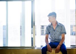 young Man sits on window sill