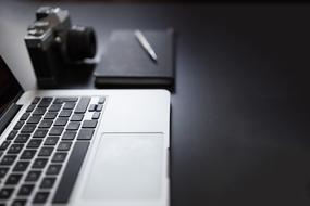 monochrome photo of laptop, retro camera and notepad on the table