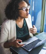 African American woman in glasses and white jacket, using laptop, at the workspace