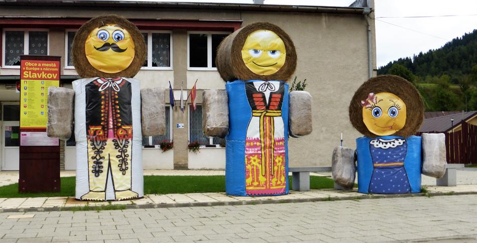 contemporary art objects in front of building, family in folk costumes