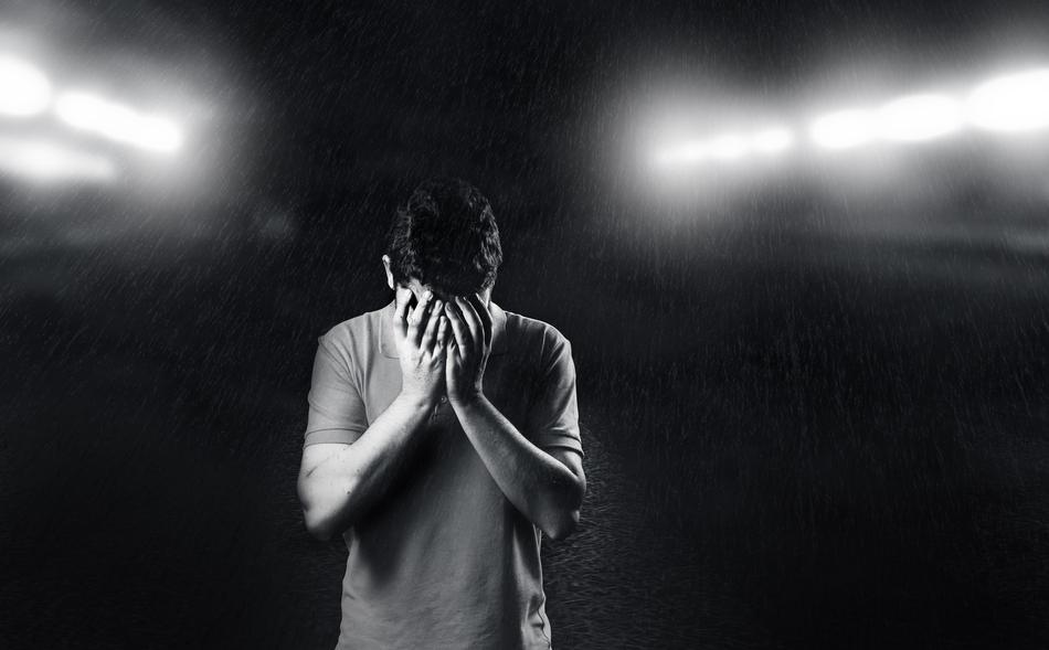 sad young man in the rain under the light of spotlights