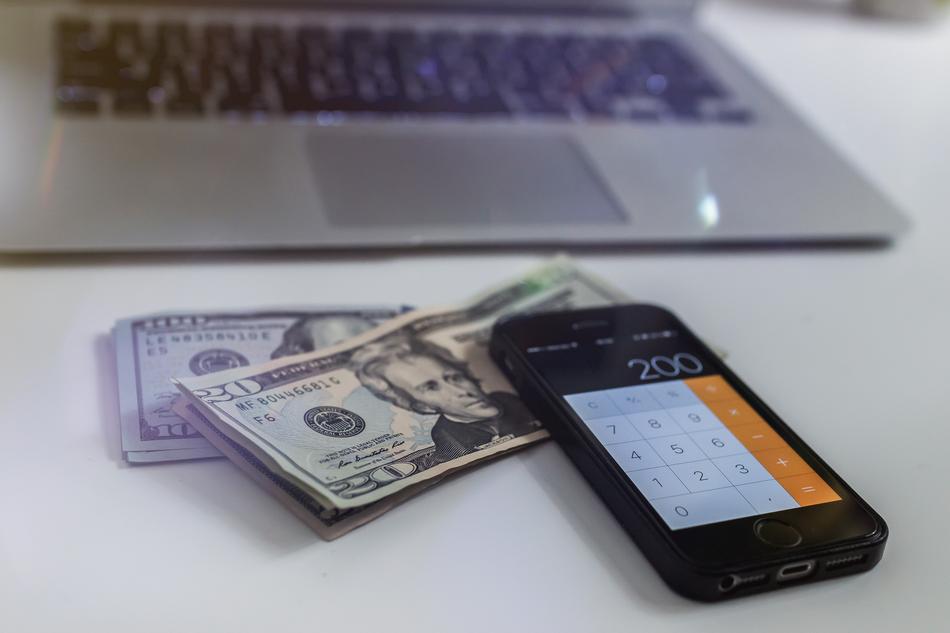 Dollar banknotes and open calculator on the smartphone, near the laptop