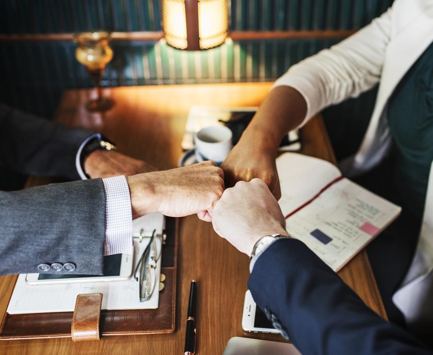 three people holding fists together above table