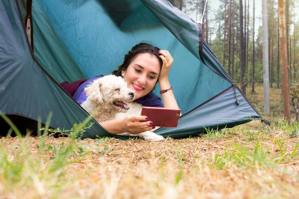 happy young girl with dog and tablet lays in tent in forest