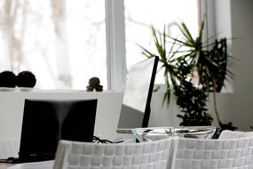 Black laptop on the white table with glass bowl, among the chairs