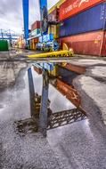 multi-colored cargo containers are reflected in a puddle