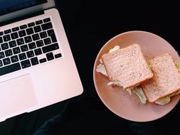 Macbook and plate with Sandwich on black desk