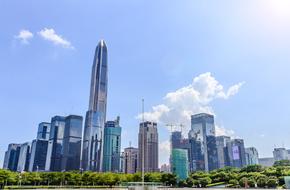 Beautiful cityscape with the shiny buildings, among the green trees, in sunlight, at blue sky with white clouds