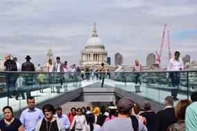 People on the Millennium Bridge, near the beautiful St Paul's Cathedra, under the blue sky with clouds