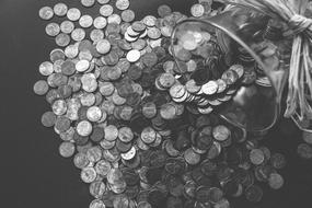 Black and white photo with the close-up of the coins pouring out of the glass piggy bank