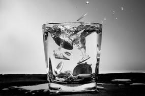 Black and white photo of the coins, falling into the whiskey tumbler of water, with the splashes