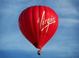 Beautiful, red hot air balloon with white "Virgin" text, at blue sky with white clouds on background