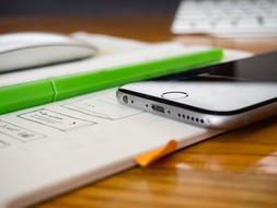 Close-up of the shiny Iphone and green pen, near the white mouse and keyboard