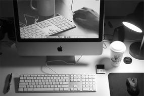 coffee cup and keyboard are reflected on the apple computer screen