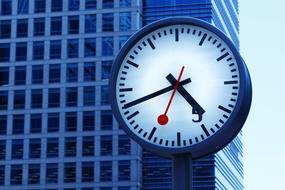 Close-up of the clock, with the arrows, near the shiny building, at blue sky on background, in London, England