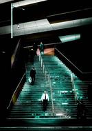 People, walking on the turquoise stairs of the building, among the darkness