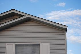 Window and roof of the house, at blue sky with white clouds on background