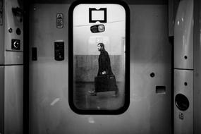 black and white photo of a man with a suitcase outside the train window