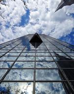 Low angle shot of the shiny building, with the windows, with the reflection of blue sky with white clouds, with sunlight