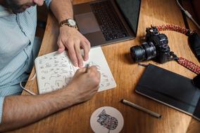 Person, drawing on the notebook, at the wooden desk