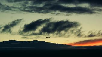 airplane in the clouds over the mountains at dusk