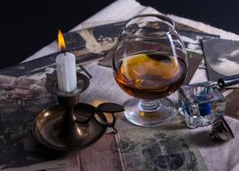 Beautiful glass of cognac and burning white candle, on the colorful, vintage cards