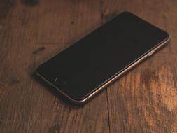 Close-up of the beautiful, dark smartphone on the wooden desk, in shadow and light