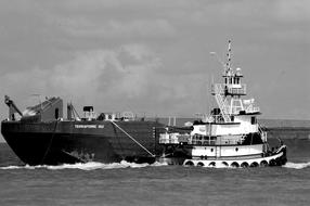 black and white photo of a tugboat near a ship in the sea