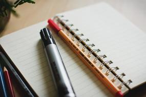 Black marker and red pen on the beautiful notebook, near the colorful pencils, on the wooden table