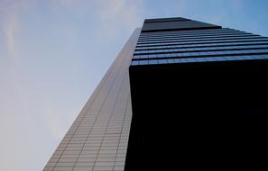 Low angle shot of the shiny skyscraper with the blue windows, under the blue sky with white clouds, in Madrid, Spain