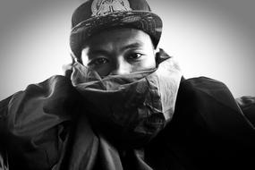 Black and white photo, with the portrait of man, covered with scarf, and in the cap