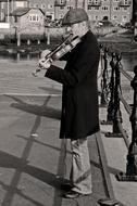 Black and white photo of the violinist, playing near the fence