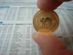 gold coin in hand over newspaper close-up