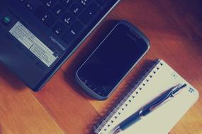 Smartphone and laptop near the notepad with pen, on the wooden desk