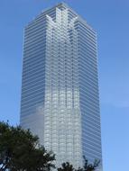 Shiny building behind the green trees, in Dallas, Texas, USA, under the blue sky