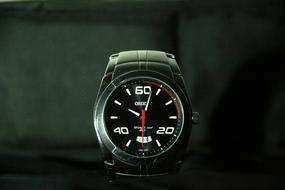 Close-up of the shiny wrist watch with the arrows, among the darkness