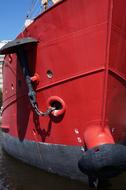 Shiny, red, metal boat with chain anchor, in sunlight, under the blue sky