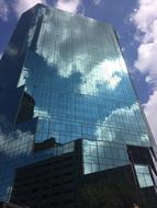 the sky and clouds are reflected in the glass skyscraper