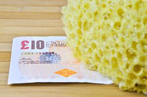 Yellow sponge in light, near the colorful banknote, on the wooden surface