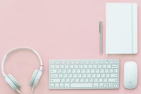 White computer accessories and notebook with a pen on a pink table