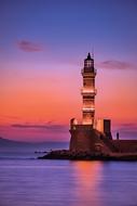 photo of a lighthouse on a background of pink-purple sunset by the sea in Greece