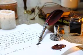 Beautiful and colorful feather with the ink in the glass, near the letters and candle, on the table, with the other stuff